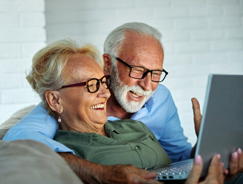 Portrait of an elderly senior happy couple using laptop at night, using modern technology having fun with glowing screen in dark office or at home, watching tv together at home. Shot of a mature activ