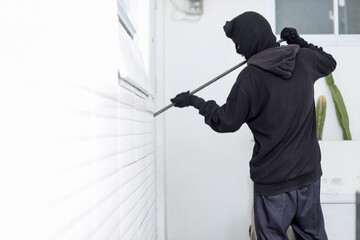Masked Thief in Black Using Crowbar to Force Open House Door During Daylight.
