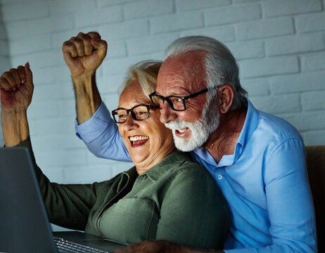 Portrait of an excited elderly senior couple watching tv on a laptop computer and screaming and cheering for their national soccer team victory, a mature aged active couple having fun using laptop at 