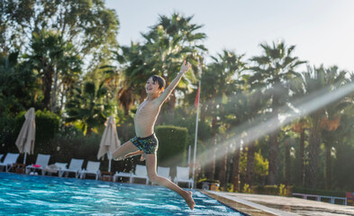 Caucasian boy kid jumping into swimming pool at summer resort, summer activity travel concept