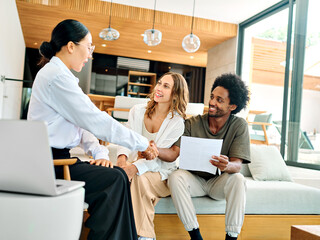Young happy couple and an agent in a new property shaking hands or with advisor in office