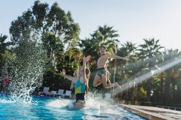 Caucasian boy and girl kids jumping into swimming pool at summer resort, summer activity travel concept