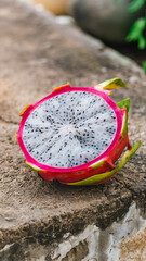 Beautifully presented half dragon fruit showcasing its vibrant pink exterior and speckled white interior. Soft texture of the fruit contrasts with rough stone surface below.