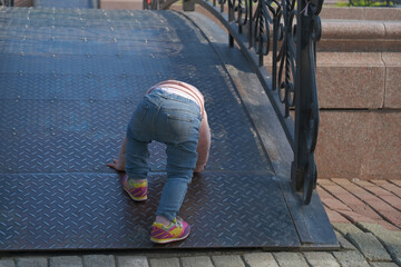 Young child in denim jeans and colorful sneakers crawls up a textured metal ramp, engaged in playful exploration and adventure, showcasing the curiosity and determination of childhood.