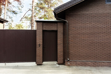 Entrance door and fence of a private brick house in the forest. Summer daytime.