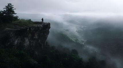 Lone traveler stands on misty cliff edge overlooking vast landscape
