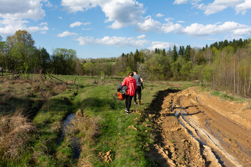 Exploring the verdant countryside under a bright sky during springtime, two adventurers wander through a muddy path lined with blooming flora and lush greenery