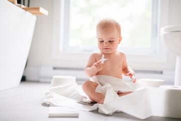 Toddler ripping up toilet paper in bathroom