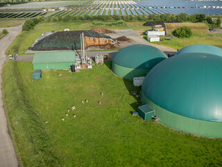Aerial view of renewable energy facility with biogas digesters surrounded by field with grazing cattle, silage storage, solar PV arrays for integrated sustainable power generation in agriculture.