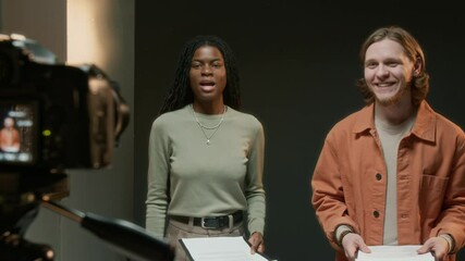 Two actors holding paper scripts and reading their lines on camera against black background in studio