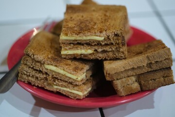 Toasted brown bread sandwiches with cheese slices stacked on a red plate, ideal for breakfast, snack, or casual meal themes.