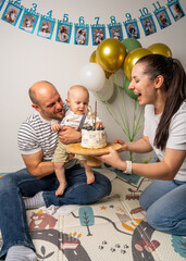 Happy father holds baby boy as mother offers birthday cake. Warm family scene full of love, joy,...