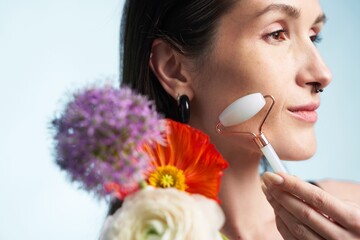 Woman using jade roller for skincare with flowers at a bright location