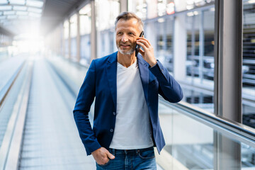 Smiling businessman with hand in pocket talking on smart phone at escalator