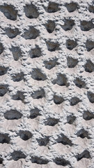 A close-up shot captures a rough, light-colored stone wall featuring a repetitive pattern of deeply...