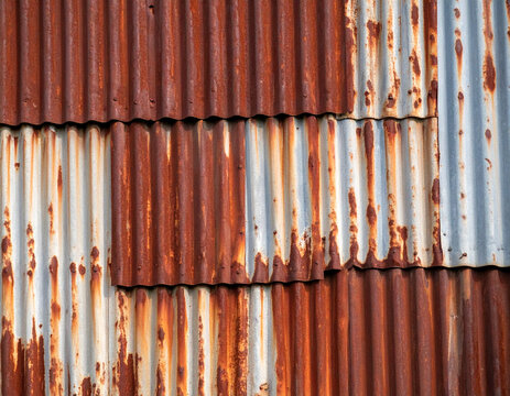 A close-up of heavily rusted corrugated iron sheets, showing peeling paint and a gritty, industrial decay. - Powered by Adobe