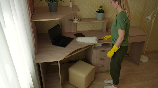 A young woman is cleaning her apartment using a duster. She uses it to dust the table. Apartment cleaning.