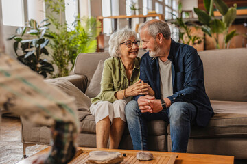 Happy senior couple holding hands and talking on sofa at home