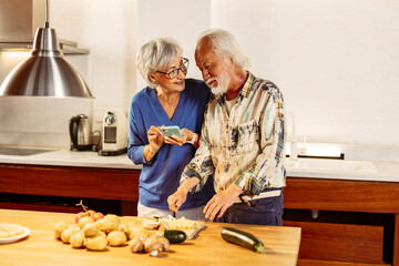 Senior couple cooking together following a recipe on smartphone