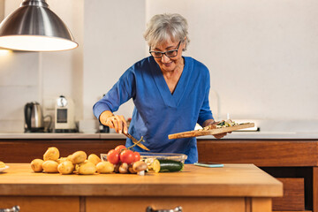 Senior woman preparing vegetables for roasting in modern kitchen