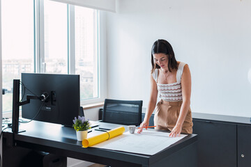 Architect leaning on desk examining blueprint in office