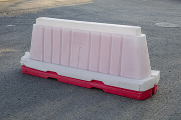 Pink and white barricade is on the ground. The barricade is made of plastic and is placed on a...