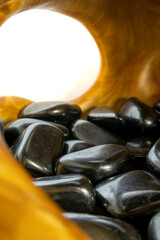 Wooden bowl filled with black stones. The bowl is open and the stones are scattered around the bowl