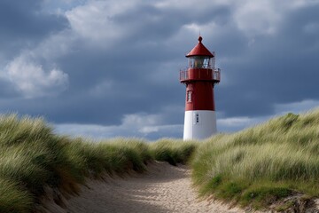 Red and white lighthouse atop a grassy dune under a cloudy sky viewed from a sandy path
