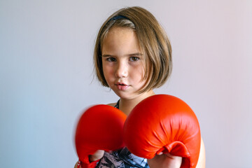 A serious young girl wearing red boxing gloves poses confidently, ready for action. Captured with...