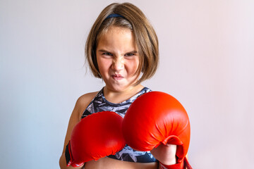 A confident young girl wearing red boxing gloves and a sporty top punches toward the camera....