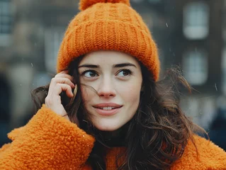 Papier peint photo intissé A beautiful young woman wears an orange knitted hat and coat while standing outside in winter weather.