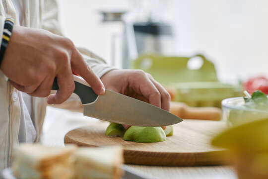 Close-up of hands cutting an apple on a wooden board in a kitchen, preparing a healthy snack.