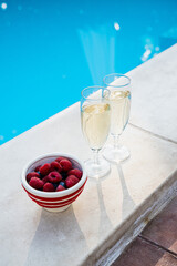 Two glasses of champagne and a bowl of fresh berries by the pool for a summer celebration