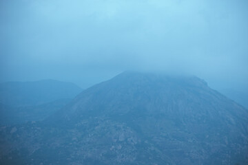 A fog-covered mountain peak in Nandi Hills, Karnataka, during early morning.

