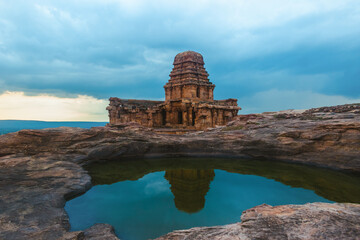 A majestic ancient temple stands on a rocky platform, reflected in the still waters of a natural...