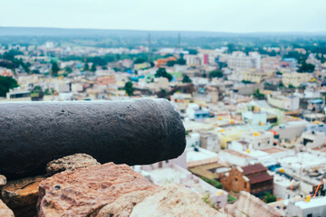 An old cannon rests on the ramparts of a historical Indian fort, aimed toward the sprawling cityscape below.