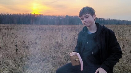 Young guy fries sausages on the nature in the evening. Bonfire in nature.