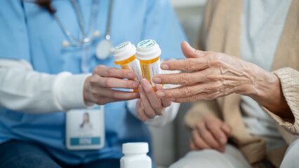 Nurse or caregiver assisting elderly woman with medication instructions during home visit or...