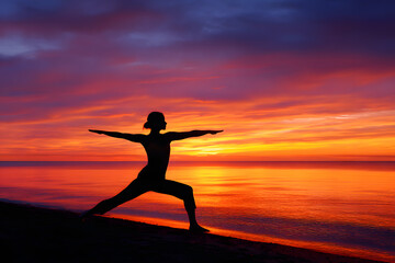 Silhouette of a woman gracefully holding the Warrior II yoga pose on a serene beach at sunset.