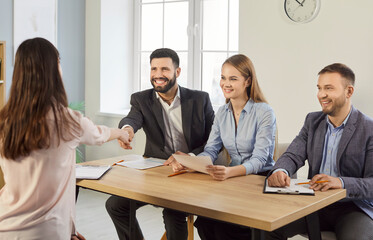 Smiling recruiters sitting at desk and shaking hands with female candidate during job interview in...