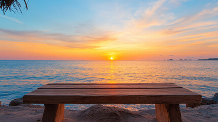 A wooden bench is on the beach with the sun setting in the background