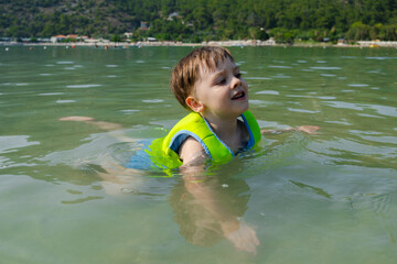 Small child swimming in life jacket in shallow water. Summer recreation