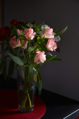 Fototapeta premium Colorful alstroemeria flowers arranged in a glass vase on a table against a dark background