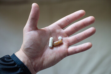 Hand holding colorful capsules and tablets on a neutral background, representing health and wellness choices