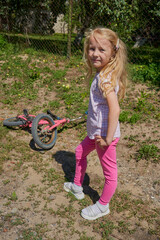 little girl standing in pink pants leggings outdoors, fashionable little girl standing in nature and in the background a bicycle lies, beautiful sunny day