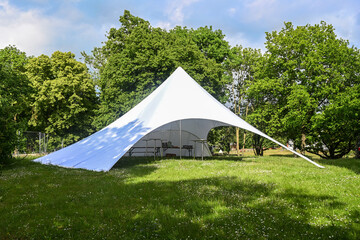 Large party tent made of white canvas with variable openings on a meadow in the park for a summer...