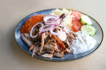 Gyros served with onions, coleslaw, rice with sauce and tzatziki on a plate in a restaurant, Greek...