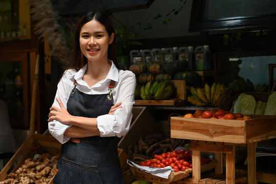 An Asian Female entrepreneur running her own organic vegetable stall, standing confidently at a fresh produce market with a display of fruits and vegetables in the background