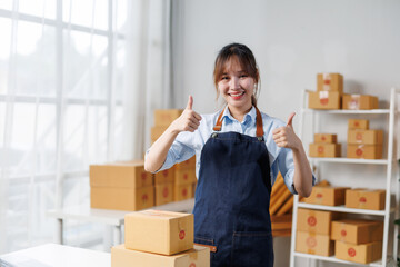 Young entrepreneur gesturing thumbs up while managing her online store and preparing packages for delivery