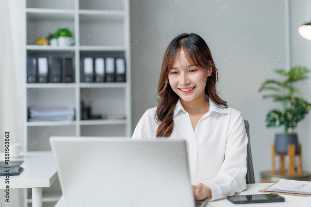 Poster happy manager working at a modern office desk, smiling while using a laptop and engaging with the sc